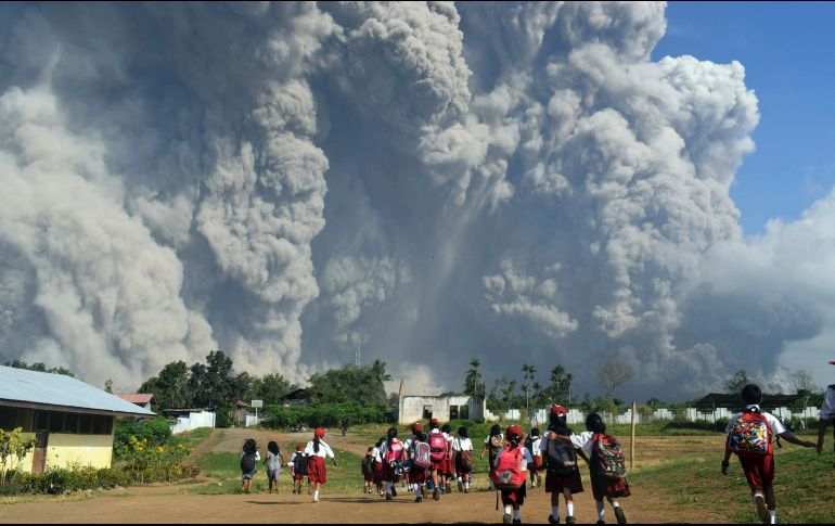 Estudiantes caminan mientras el monte Sinabung registra una erupción en Karo, Indonesia. El volcán ha arrojado columnas de ceniza de más de cinco mil metros. AP/Sarianto