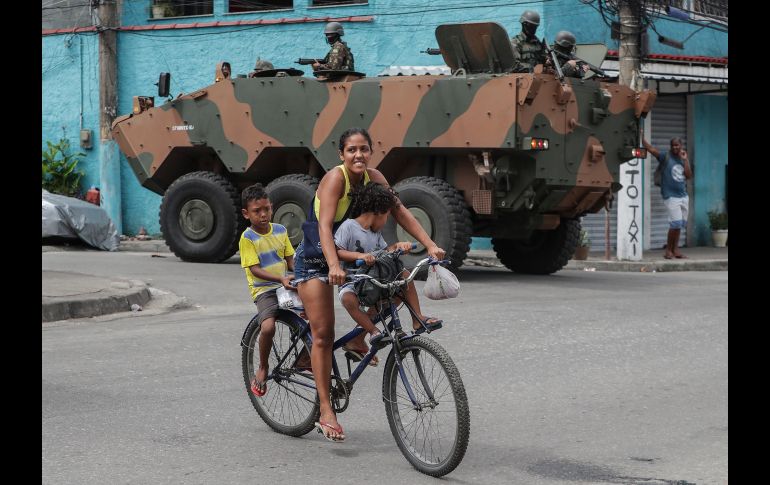 Una mujer transporta dos niños en bicicleta mientras militares realizan un operativo en las favelas de Vila Aliança y Coreia, en Río de Janeiro, Brasil. EFE/ A. Lacerda