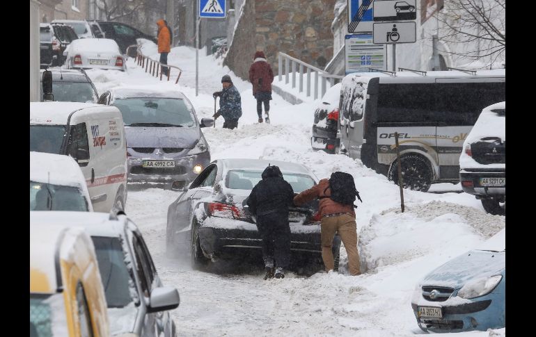 Varias personas empujan un coche atrapado por la nieve en el centro de Kiev, Ucrania. La ola de frío que golpea Europa desde hace varios días sigue causando afectaciones por vientos y nevadas