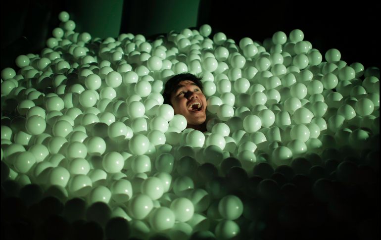 Un hombre reacciona en un juego de pelotas de plástido en un parque de instalaciones inflables a gran escala, parte del festival 