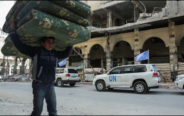 Un niño carga colchones mientras vehículos de la ONU y del Comité de la Cruz Roja Internacional entregan ayuda humanitaria en la ciudad siria de Douma. AFP/H. Al-Ajweh