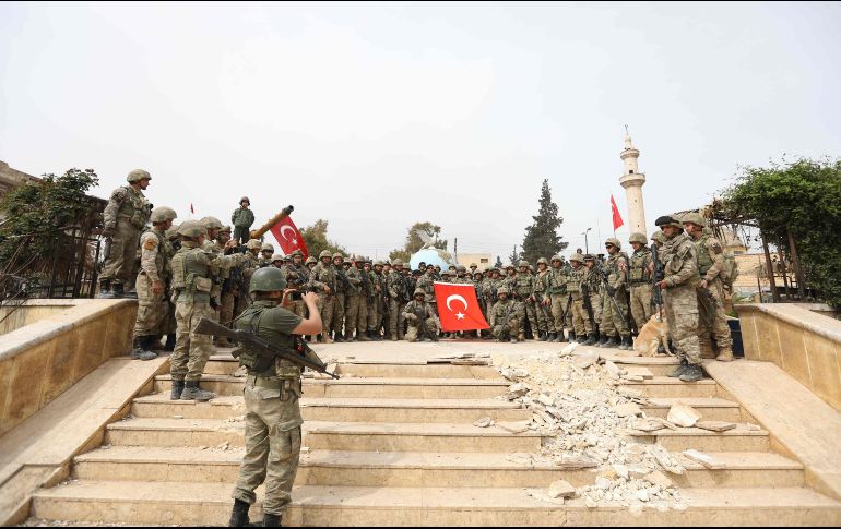 Varios soldados turcos posan con una bandera entre las ruinas de un edificio. AFP/O. Haj Kadour