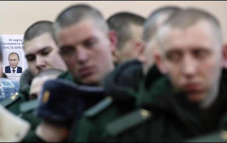 Un póster del presidente ruso  Vladimir Putin se ve en una pared mientras soldados hacen fila para votar en las elecciones presidenciales en San Petersburgo. Putin busca reelegirse para un cuarto mandato. AP/D. Lovetsky