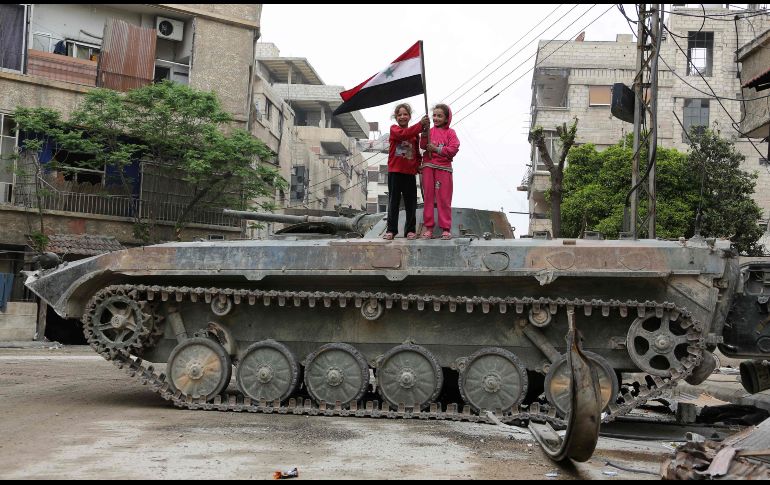 Niñas sostienen una bandera siria arriba de un tanque en Hazzeh, en la región de Guta del Este. AFP