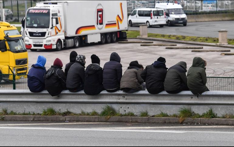 Migrantes se sientan en una barrera contra choques, en una vía que conduce al puerto en Calais, Francia. AFP/D. Charlet