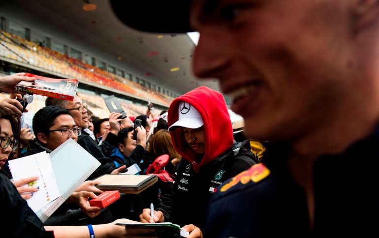 Lewis Hamilton (c), piloto de Mercedes, firma autógrafos junto a Max Verstappen (d), de Red Bull, previo al Gran Premio de Fórmula 1 de China, en Shanghái. AFP/J. Eisele