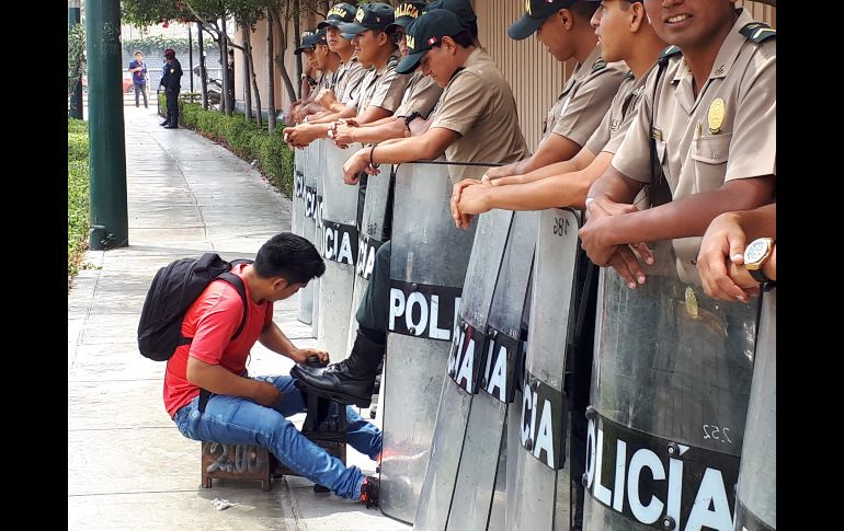 Un chico que limpia calzado, da servicio a un policía que resguarda el ingreso de la sede de la VIII Cumbre de las Américas, en Lima, Perú. EFE / E. Levy