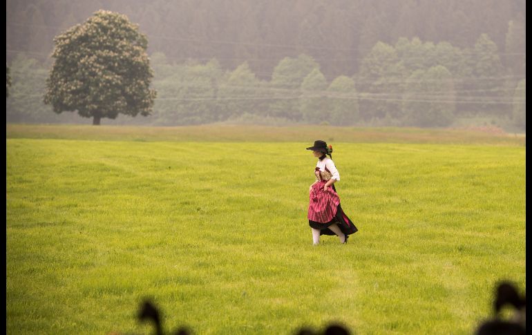 Una mujer vestida con un traje tradicional atraviesa una pradera para asistir a la celebración del Día del Patrón de las asociaciones bávaras de tiro, en Bichl, Alemania. EFE/L. Barth