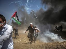 Manifestantes corren para protegerse del gas lacrimógeno lanzado por soldados israelíes durante unas protestas en la frontera de Gaza e Israel. EFE/M. Saber