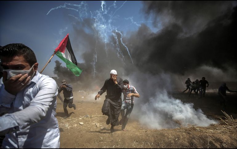 Manifestantes corren para protegerse del gas lacrimógeno lanzado por soldados israelíes durante unas protestas en la frontera de Gaza e Israel. EFE/M. Saber