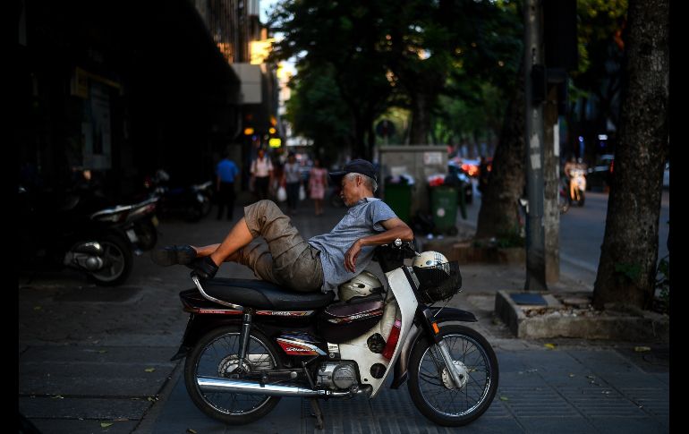 Un hombre toma una siesta en su motocicleta, colocada junto a una calle en Hanoi, Vietnam. AFP/M. Vatsyayana