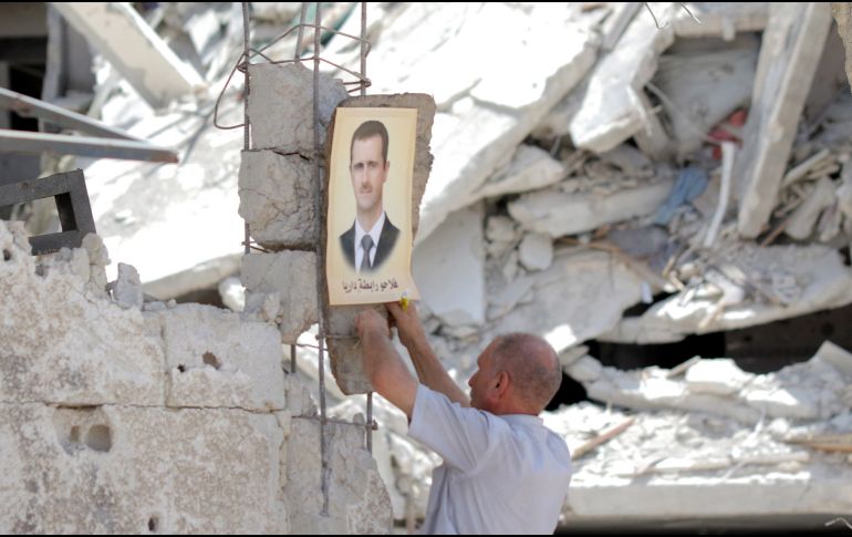 Un hombre coloca una imagen del presidente sirio, Bachar Al Assad, en un edificio dañado durante una celebración en el barrio al-Hajar al-Aswad, recuperado por el gobierno, en Damasco, Siria. EFE/ Y. Badawi