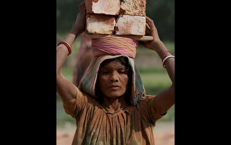 Un mujer carga ladrillos sobre la cabeza mientras trabaja en una fábrica en Nagda, India. EFE/P. Adhikary