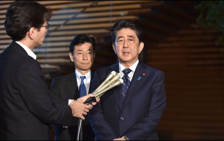 Shinzo Abe (d) responde a las preguntas de varios reporteros en su residencia oficial de Tokio, antes de partir al aeropuerto. AFP/K. Nogi