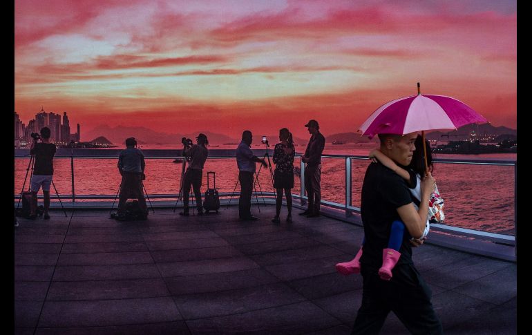 Un hombre con paraguas pasa junto a un póster de una puesta de Sol en Hong Kong. AFP/P. Fong