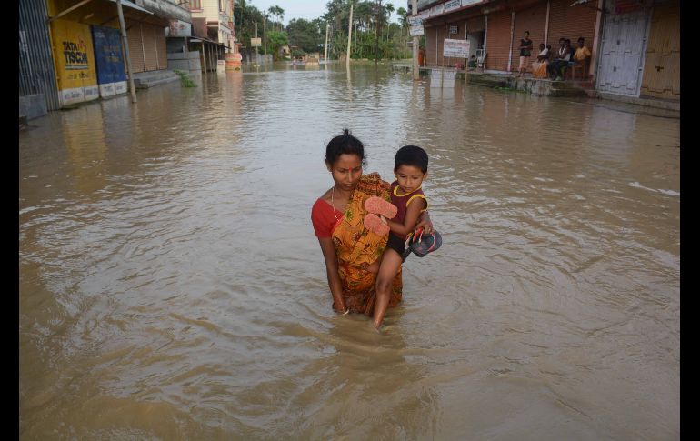 Una mujer carga a un niño en una calle inundada tras fuertes lluvias en Baldakhall, India. AFP/A. Dey