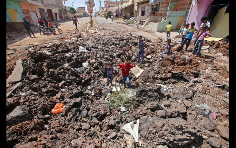 Niños posan para una foto dentro de un hoyo dejado por un bombardeo en Deraa, Siria. Las negociaciones entre Rusia y representantes de las facciones opositoras sirias en esta provincia sobre el control de los últimos territorios en manos rebeldes en esta zona han fracasado. AFP / Y. Karwashan