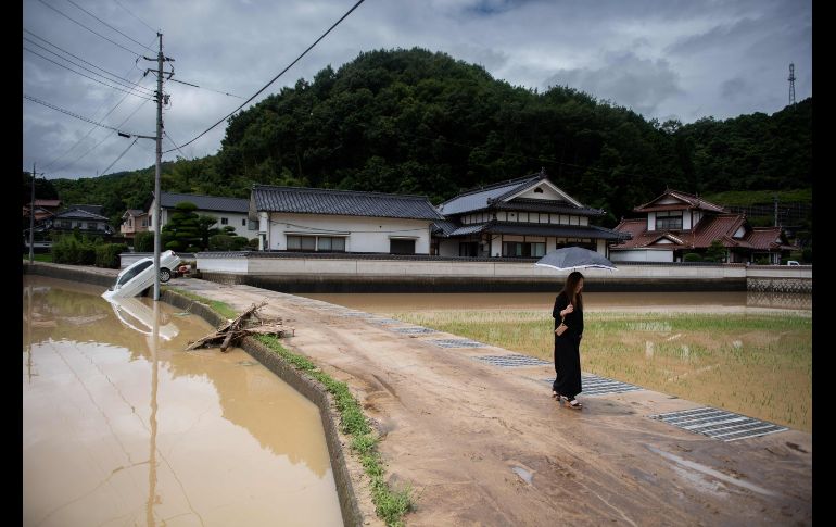 Una mujer pasa junto a campos de arroz inundados en Mihara, Japón, tras lluvias torrenciales. AFP/M. Bureau
