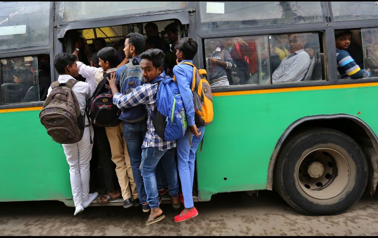 Estudiantes cuelgan de la puerta de un autobús en la hora pico de tráfico matutino en Bangalore, India. AP/A. Rahi