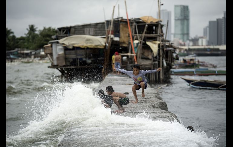 Niños que viven en casas sobre el malecón juegan con las olas en Manila, Filipinas, que resiente los efectos de la depresión tropical 