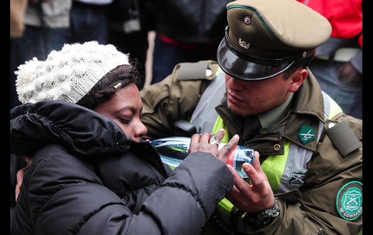 Una haitiana bebe agua tras sufrir un desmayo debido al frío y a las horas de espera frente a la embajada de Haití en Santiago, Chile. Cientos de haitianos hacen fila desde hace días en busca de regularizar su situación en el país suramericano antes de que el lunes se cumpla el plazo y queden como inmigrantes irregulares. EFE/A. Valdés