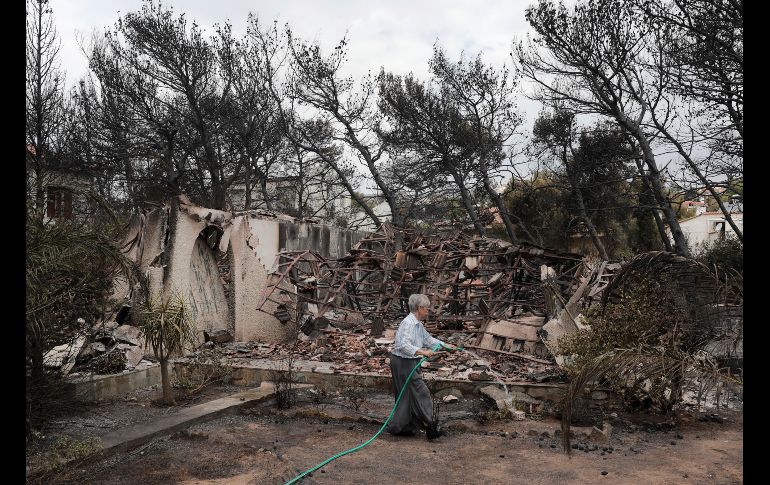 Una mujer arroja agua en su casa afectada por un incendio forestal en Neos Voutzas, Grecia. AP/Y. Karahalis