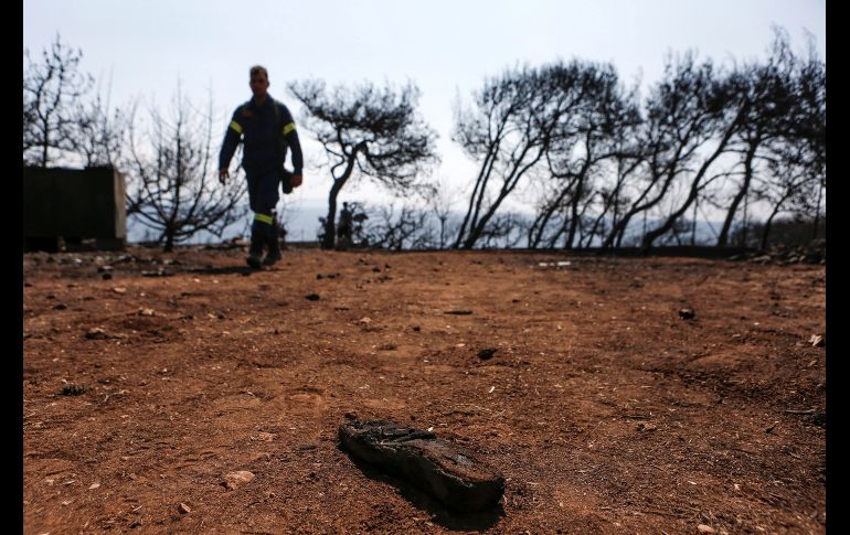 Un elemento de los servicios de emergencia pasa cerca de una sandalia en el lugar donde se encontraron 26 cadáveres calcinados, tras el incendio registrado en Mati, Grecia. La cifra de muertos por los incendios que han asolado la costa al noreste de Atenas suma 79. EFE/ Y. Kolesidis