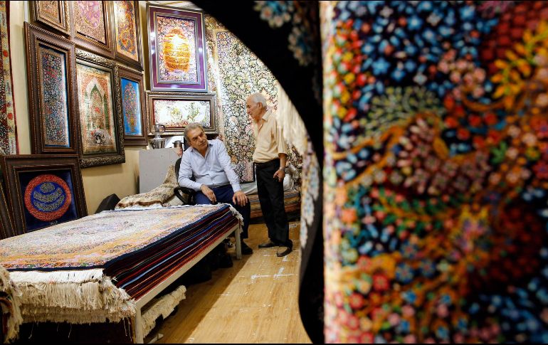 Dos hombres iraníes conversan dentro de su negocio de alfombras en el Gran Bazar de Teherán. La importación de estos productos se verá afectada con la medida. EFE/A. Taherkenareh