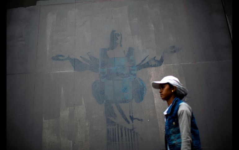 Una mujer camina frente a un grafitti de la estatua del Cristo Redentor con un chaleco antibalas, en una pared del teatro Joao Caetano en Río de Janeiro, Brasil. AFP/M. Pimentel