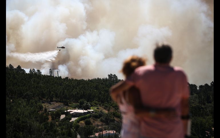 Una pareja observa un helicóptero que arroja agua sobre un incendio en Monchique de Algarve, Portugal. El incendio afecta desde el viernes a la región del Algarve. AFP/C. Costa