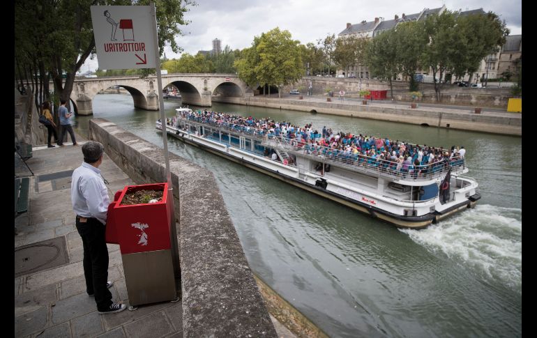 Un hombre se para en un urinario público en París, mientras pasa una embarcación turística. La capital francesa ha comenzado pruebas con los 