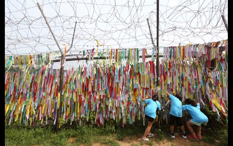 Estudiantes de primaria observan a través de una reja decorada con listones que llevan mensajes de deseos de reunificación de las dos Coreas en Paju, Corea del Sur. AP/Ahn Young-joon