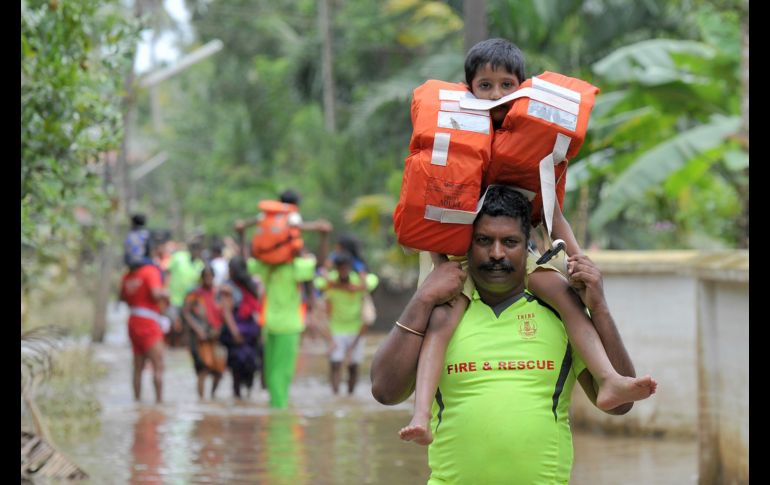 Bomberos cargan niños a través de una zona inundada en Annamanada, India. Más de 370 personas han muerto en el estado de Kerala a causa de las lluvias torrenciales que no dan tregua. AFP/M. Kiran