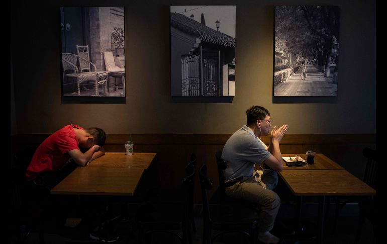 Un hombre toma una siesta mientras otro habla en su celular dentro de una cafetería en Pekín, China. AFP/N. Asfouri
