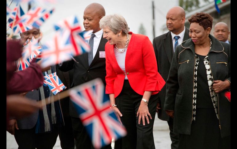 Niños con banderas británicas y sudafricanas saludan a la primera ministra británica Theresa May (c), durante una visita a una escuela en Gugulethu, Sudáfrica. May está de gira por tres naciones africanas. AFP/R. Bosch