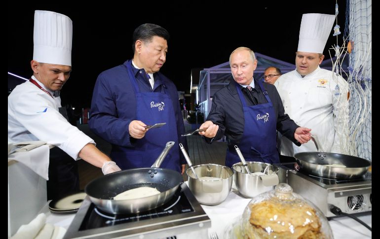 El presidente ruso, Vladímir Putin (d), y su homólogo chino, Xi Jinping (i), cocinan hotcakes durante su visita a una muestra gastronómica, durante el Foro Económico Oriental que se celebra en Vladivostok, Rusia. AFP/TASS Host Photo Agency/S. Bobylov