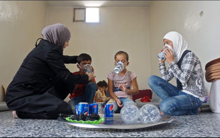 Una mujer le prueba a uno de sus hijos una de las máscaras, elaboradas con materiales reciclados. AFP/M. Haj Kadour