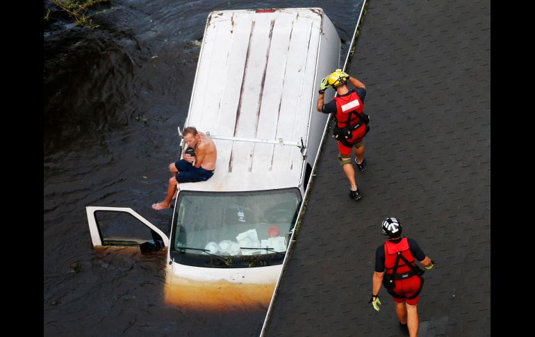 Rescatistas se acercan a Randy Haba, quien aguarda sobre un vehículo tras quedar varado por las inundaciones provocadas por el paso del 