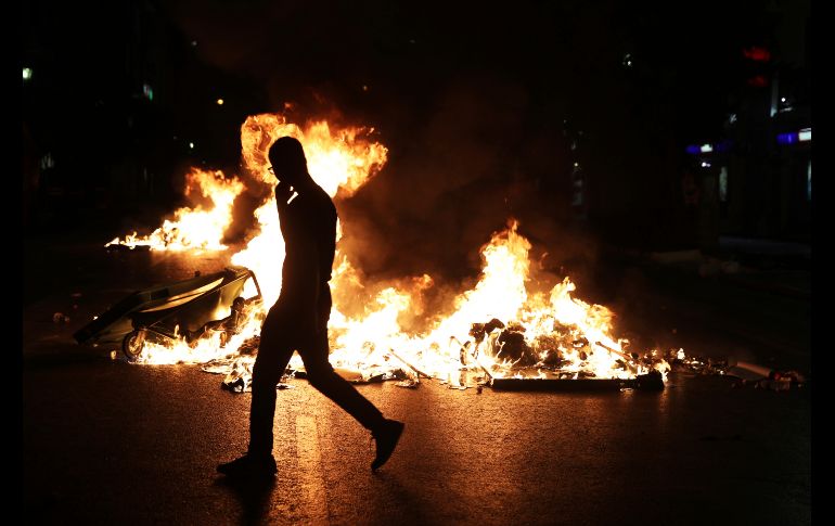 Un hombre camina frente a botes de basura en llamas, durante una protesta en El Pireo, Grecia, en el marco del quinto aniversario del asesinato del rapero  Pavlos Fyssas, que desató medidas severas contra el partido de extrema derecha Golden Dawn. AP/P. Giannakouris