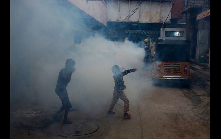 Un joven se cubre y otro baila mientras se realiza una fumigación en una colonia en Hyderabad, India, como medida contra las enfermedades transmitidas por mosquitos. AP/M. Kumar