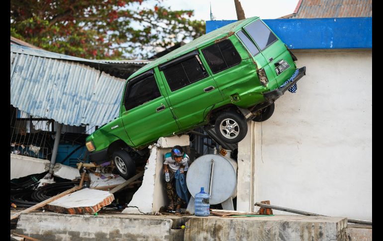Un habitante pasa debajo de un auto atorado en un edificio en Palu, Indonesia, tras el temblor y el tsunami que azotaron la ciudad el viernes. AFP/J. Samad