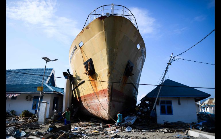 Sobrevivientes se abren paso entre los escombros y un barco de pasajeros que quedó en tierra en Wani, Indonesia, tras el sismo y el tsunami del 28 de septiembre. AFP/J. Samad
