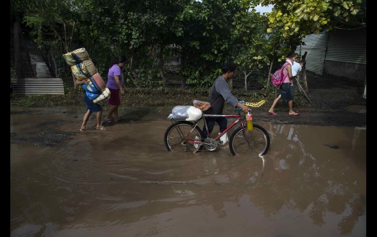 Varias personas caminan con frazadas y provisiones por una calle inundada después de que un cauce se desbordara. EFE / J. Torres