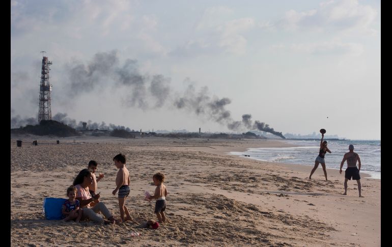 Israelíes disfrutan la playa en Zikim, cerca de la frontera entre Israel y Gaza. Al fondo se eleva humo de llantas quemadas durante una protesta de palestinos cerca de Beit Lahiya, en la Franja de Gaza. AP/O. Bality