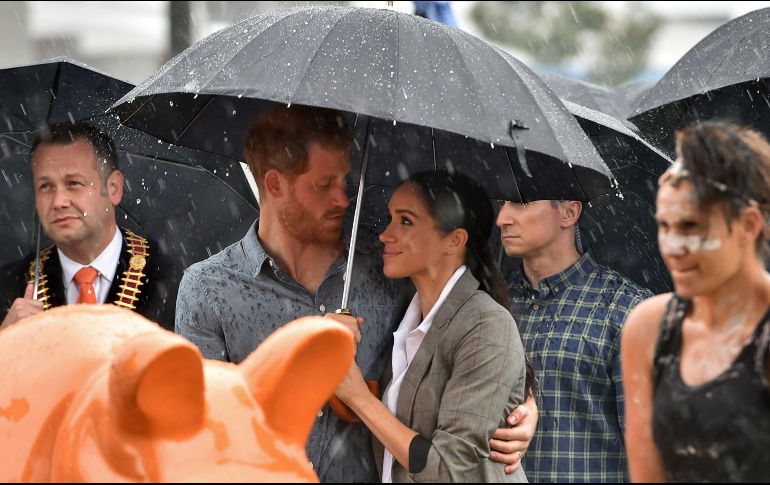 El príncipe Enrique y su esposa Meghan se cubren de la lluvia en un evento en el parque Victoria en Dubbo, Australia. La pareja real empezó el lunes en Sídney una gira de 16 días en el Pacífico. AFP/P. Parks