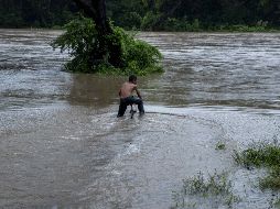 Un niño intenta cruzar con una bicicleta un río crecido por las fuertes lluvias, en la comunidad de las Banderas. EFE/J. Torres