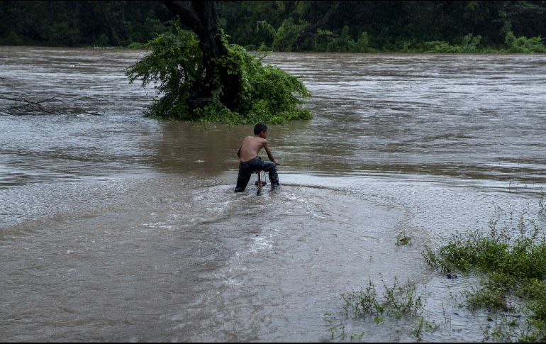 Un niño intenta cruzar con una bicicleta un río crecido por las fuertes lluvias, en la comunidad de las Banderas. EFE/J. Torres