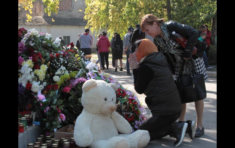 Una mujer ora junto a flores y recuerdos colocados en memoria de las víctimas de un ataque en una escuela vocacional en Kerch, Crimea. Un estudiante mató ayer a 20 personas en la escuela. AP