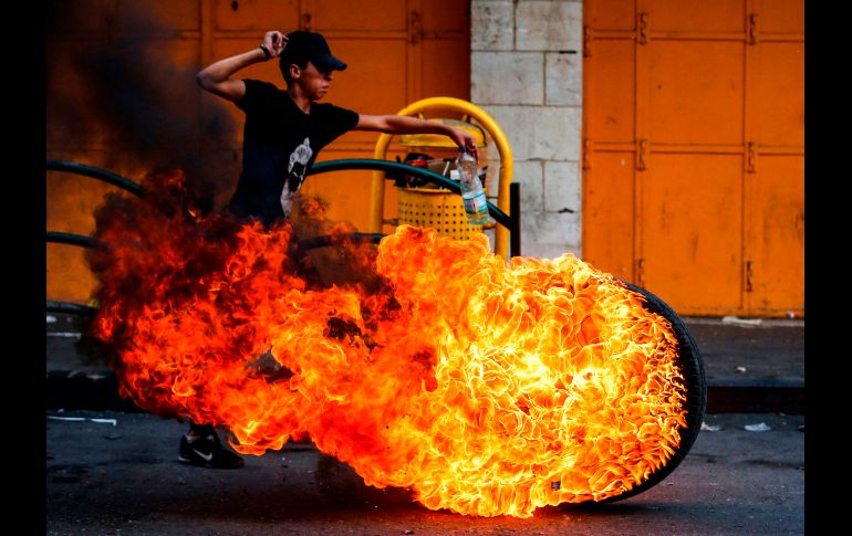 Un joven palestino pasa junto a una llanta en llamas, durante enfrentamientos con fuerzas israelíes en Hebrón, Cisjordania. AFP/H. Bader