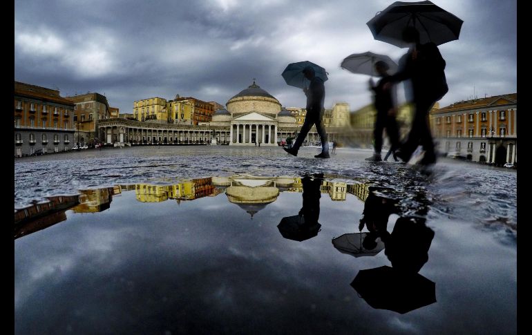 Personas se reflejan en un charco mientras llueve en el centro de Nápoles, Italia. EFE/C. Fusco